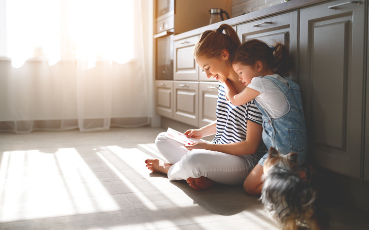 Mother and daughter enjoying story time together on the kitchen floor with sunlight streaming through the window.